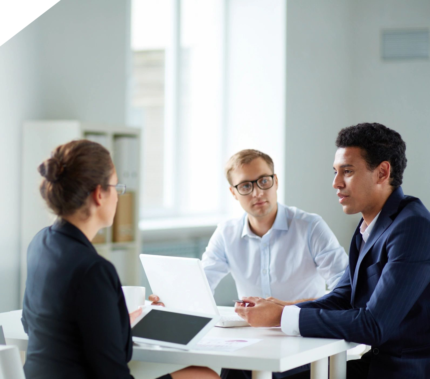 Three people sitting at a table with one of them holding a laptop.